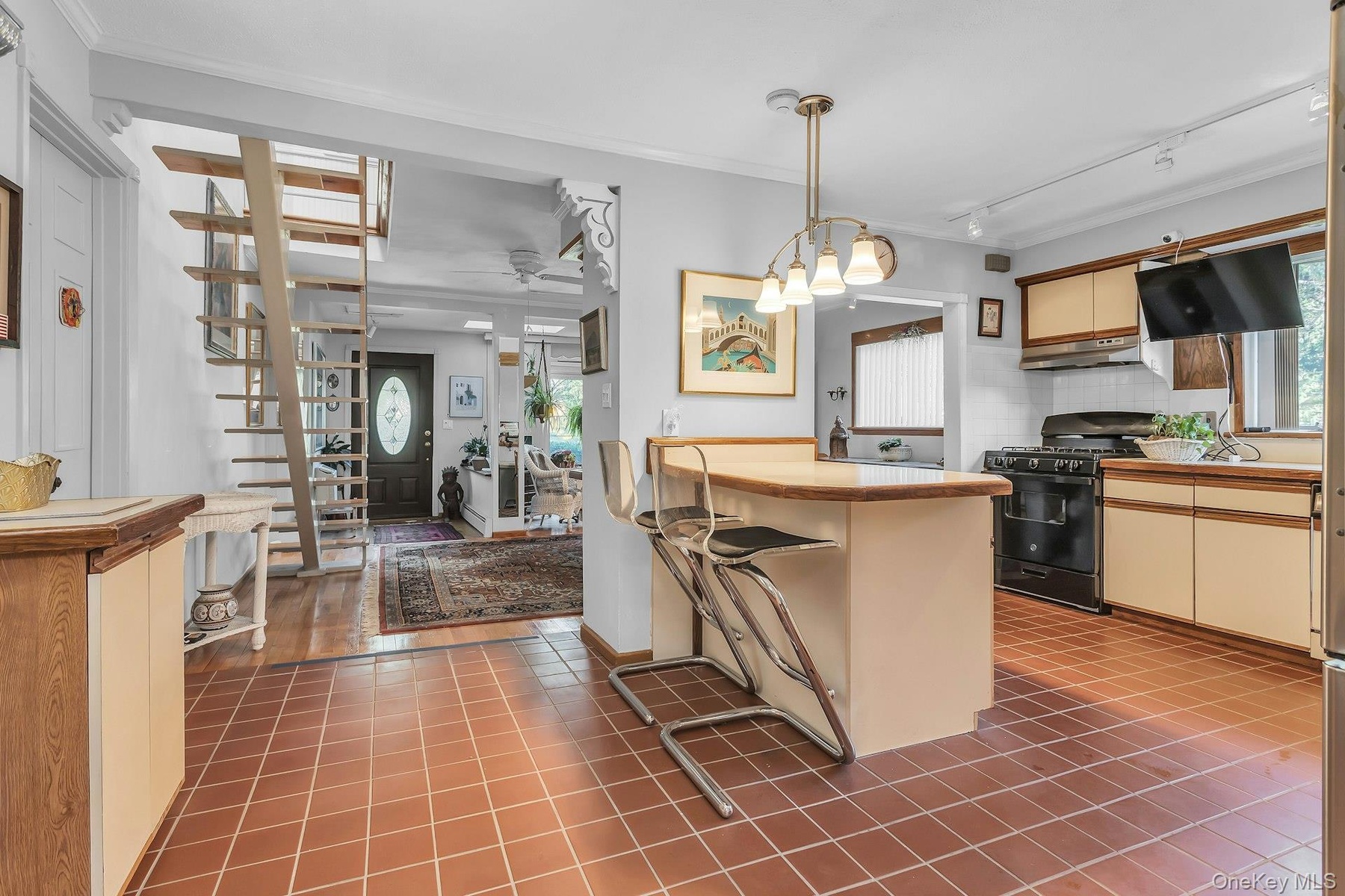Kitchen featuring terracotta-style tile flooring, a peninsula with an integrated breakfast bar, a gas range, and wood-finish cabinetry