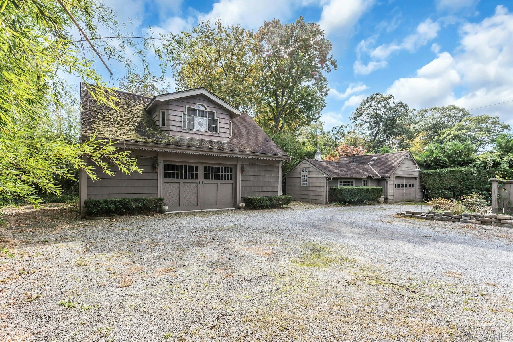 Gravel driveway with two detached structures featuring shingle siding and dormer window accents