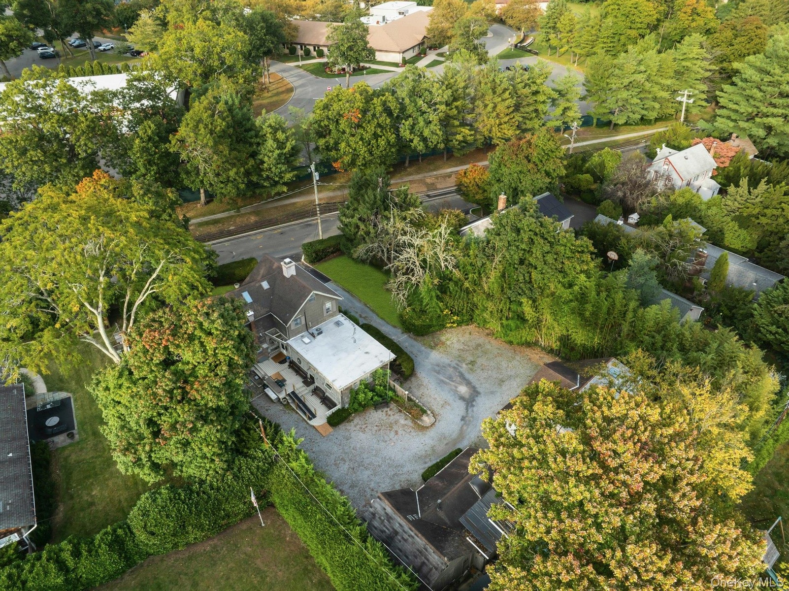 Aerial perspective of the property featuring a gravel driveway, lush green landscaping, mature trees, and a dark gray exterior home