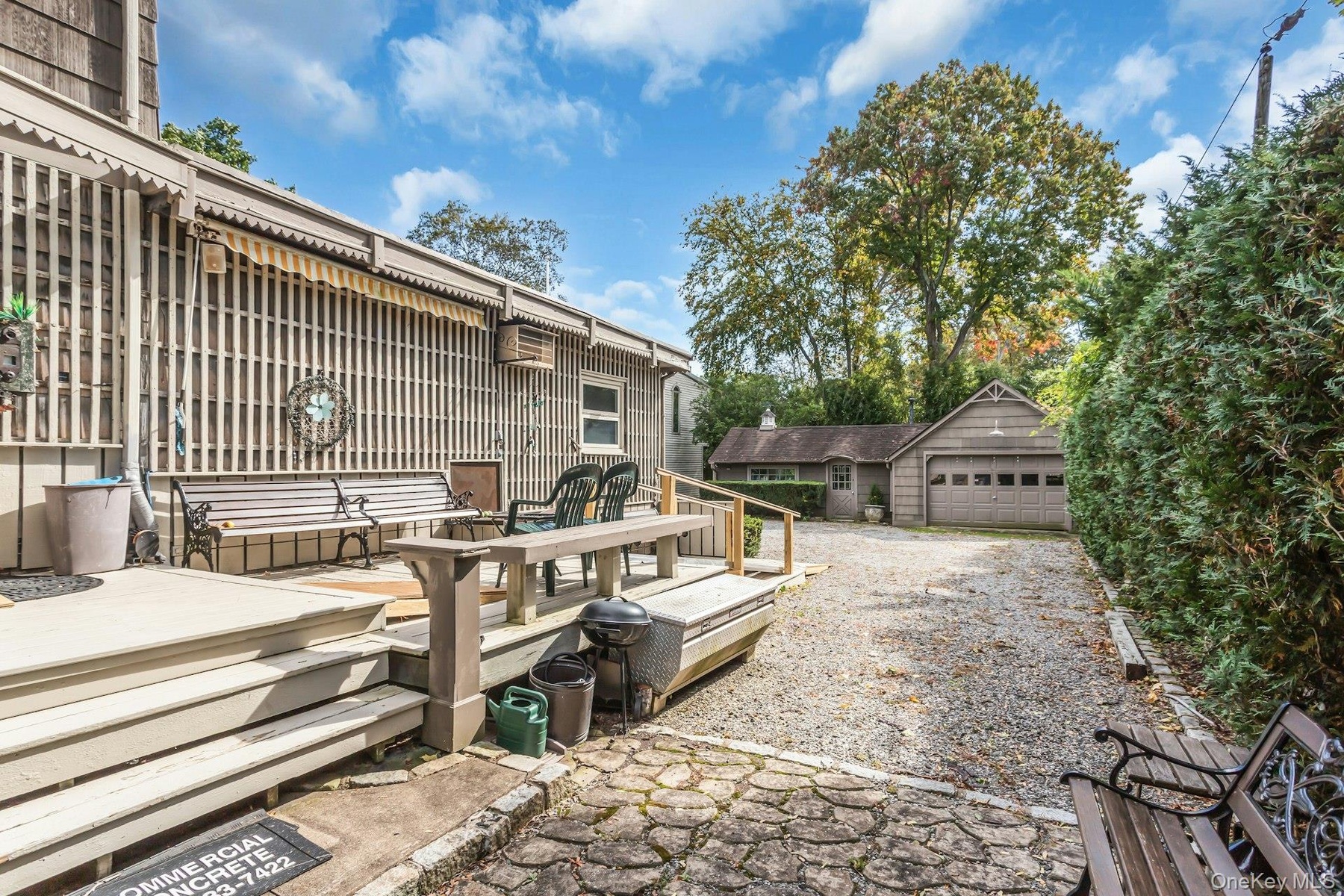 Outdoor deck with stairs, gravel driveway, detached garage, and mature perimeter landscaping