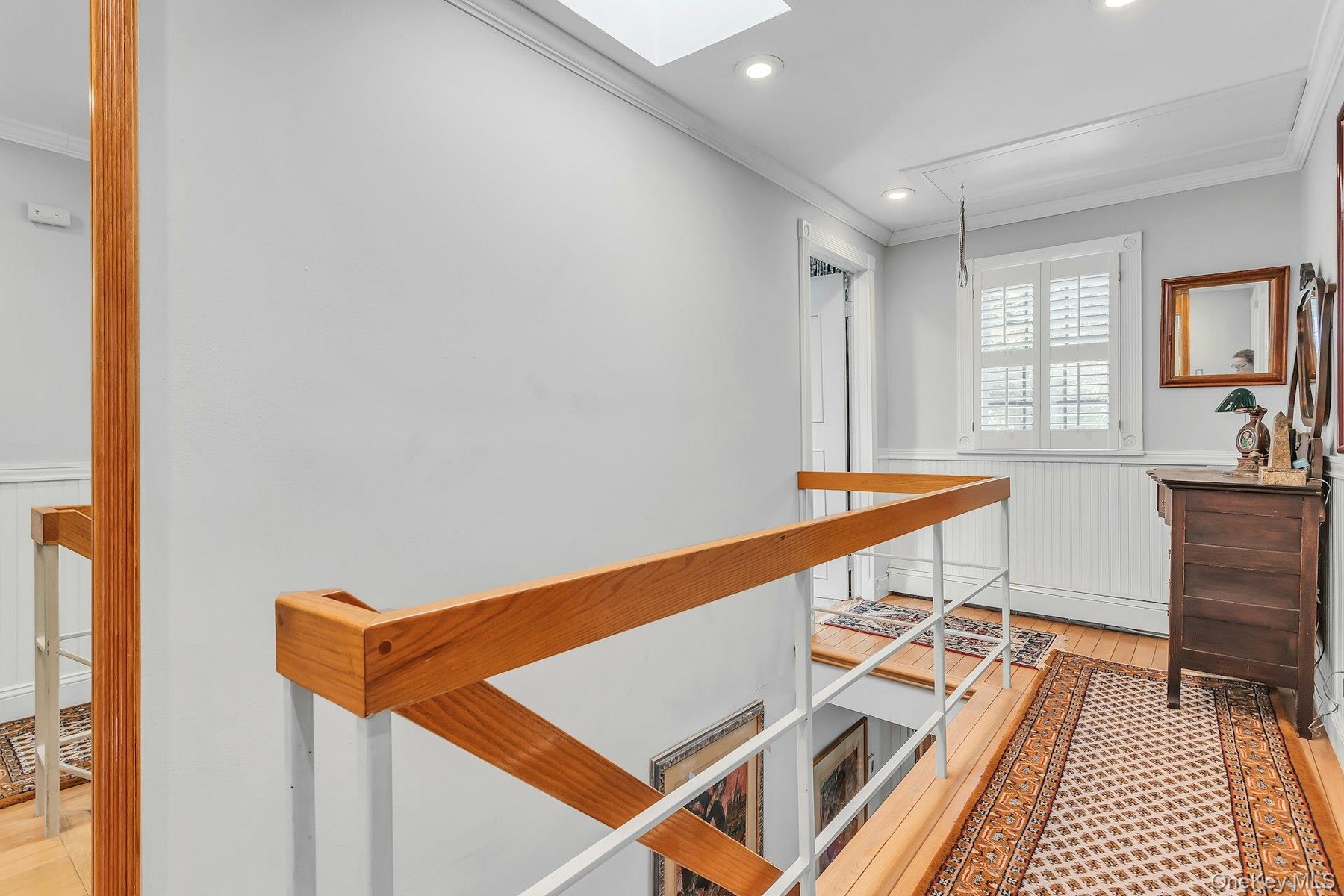 Natural wood flooring with a white wood-panel accent wall and white plantation shutters