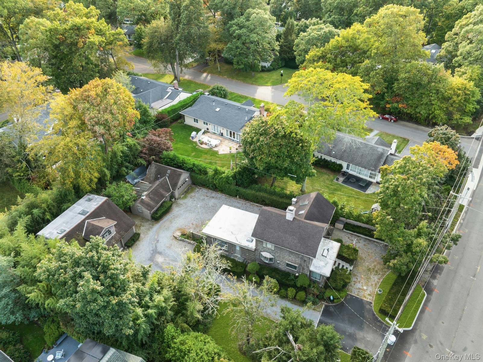 Stone facade residence featuring a dark shingle roof, extensive paved driveway, mature landscaping, and an attached garage