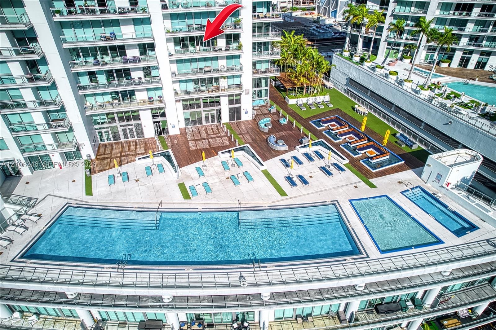 Elevated terrace balcony featuring floor-to-ceiling glass panel doors, exterior swimming pool, multi-level sundeck, and landscaped grounds