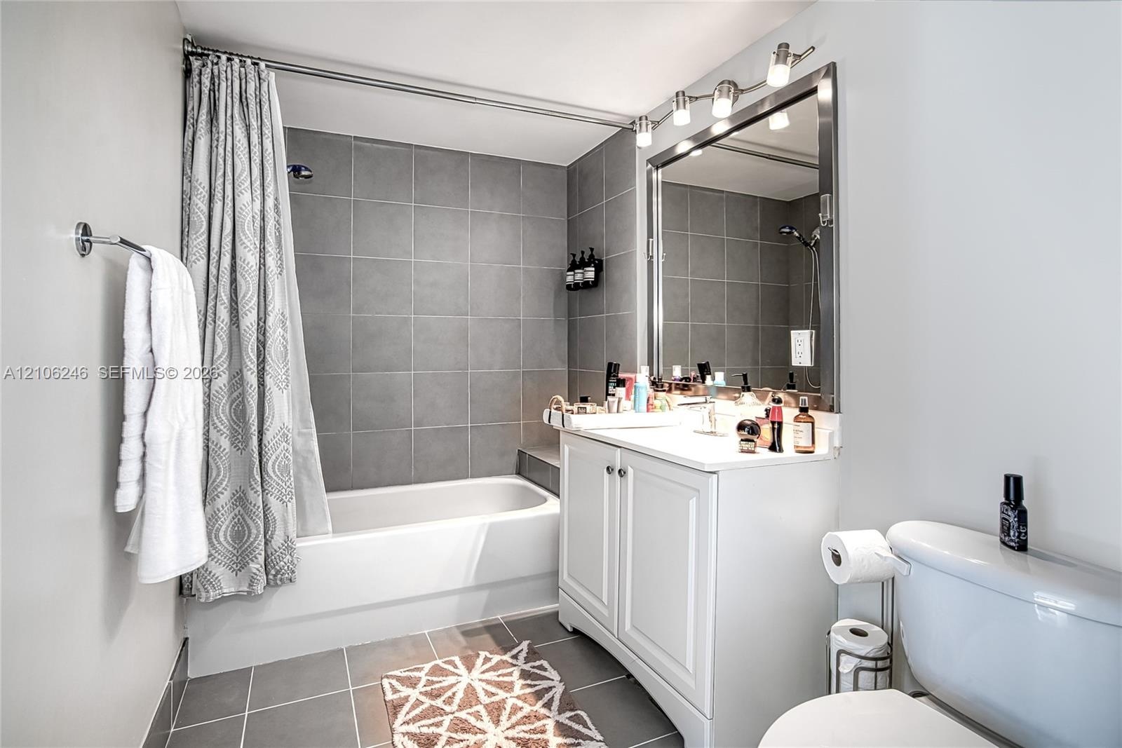 Bathroom featuring a white vanity cabinet with a solid surface countertop, an expansive framed vanity mirror, multi-bulb overhead lighting, and a show