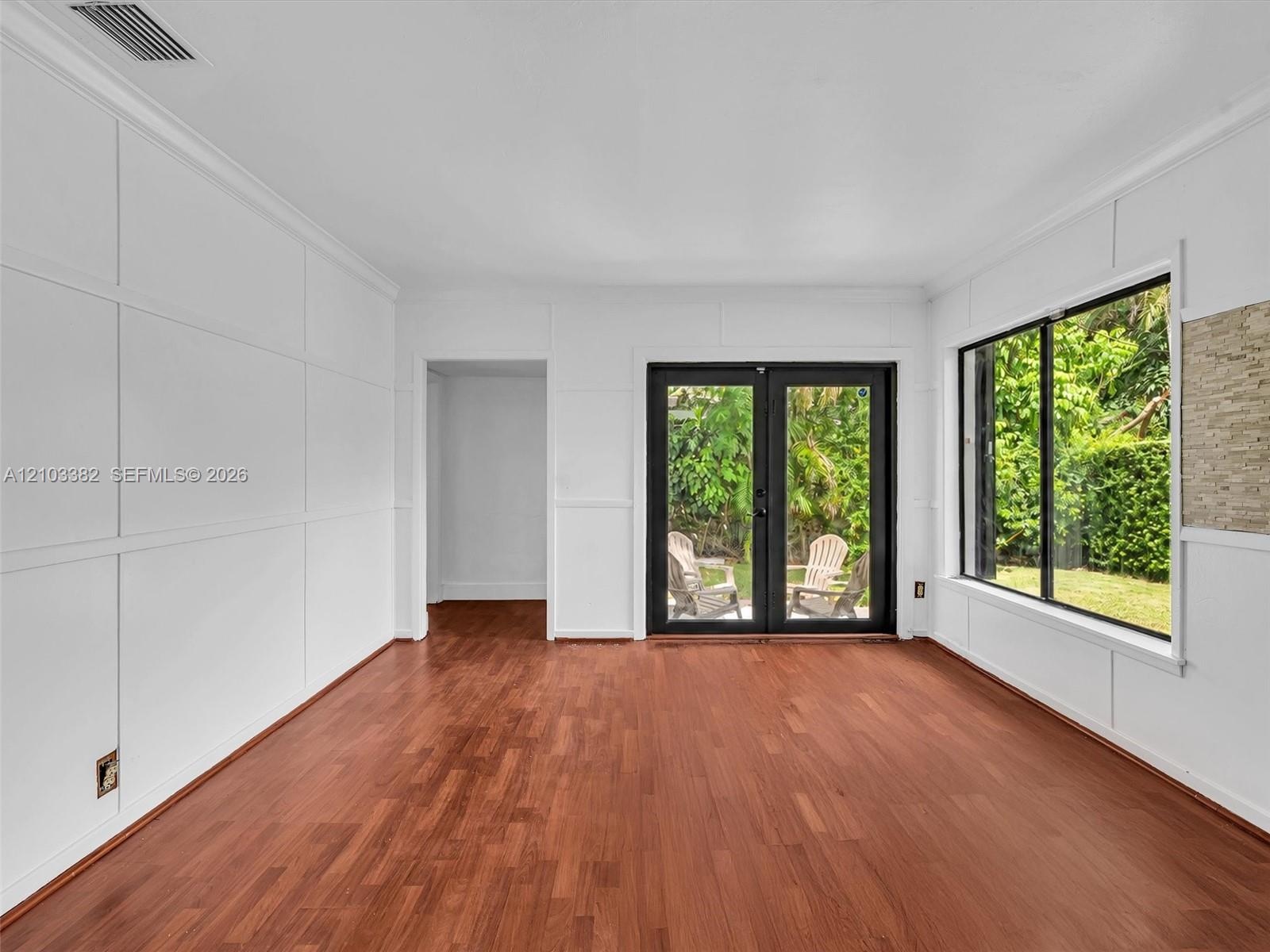 Awesome Florida room featuring wood-finish flooring, custom wall paneling, expansive windows, and black-framed double doors. House for rent in Coral G