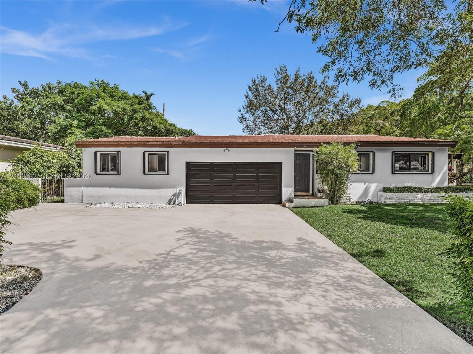 Single-story exterior featuring white stucco siding, a flat roofline, attached multi-car garage, concrete driveway, and manicured lawn. House for rent