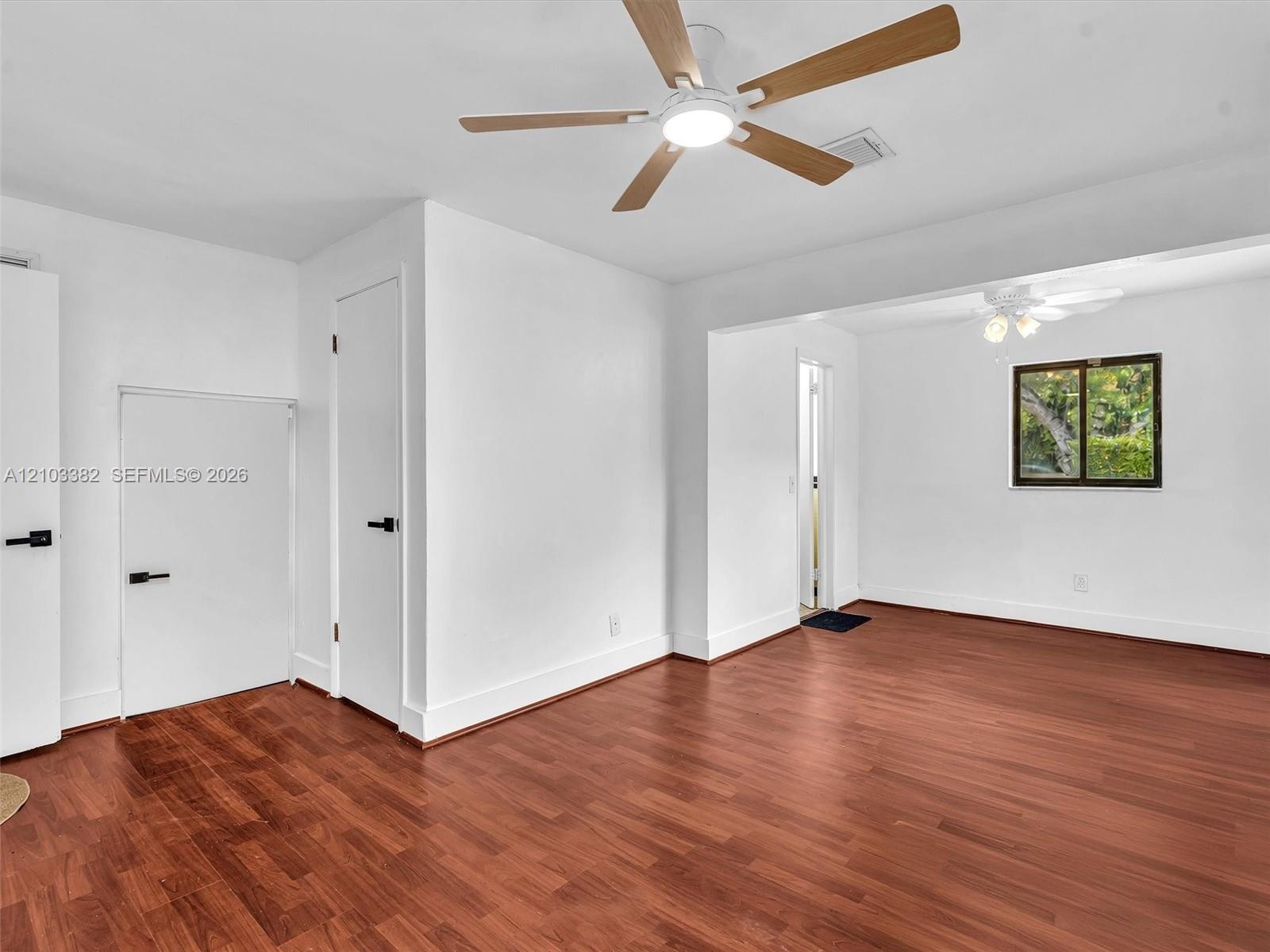 Primary bedroom featuring wood-finish flooring, two ceiling fans with integrated lighting, and doors accented with matte black hardware. House for ren