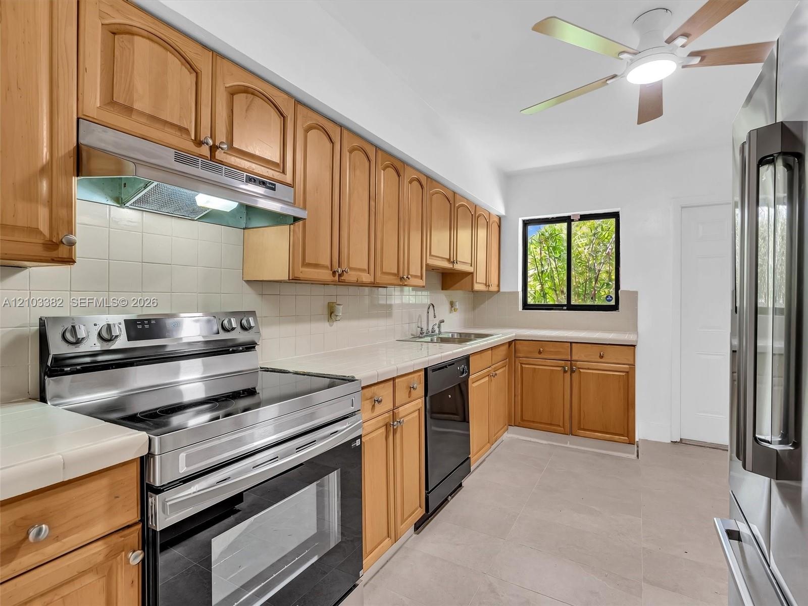 Spaceous kitchen featuring tile countertops, stainless steel appliances, a ceiling fan with integrated lighting, and tile flooring. House for rent in 
