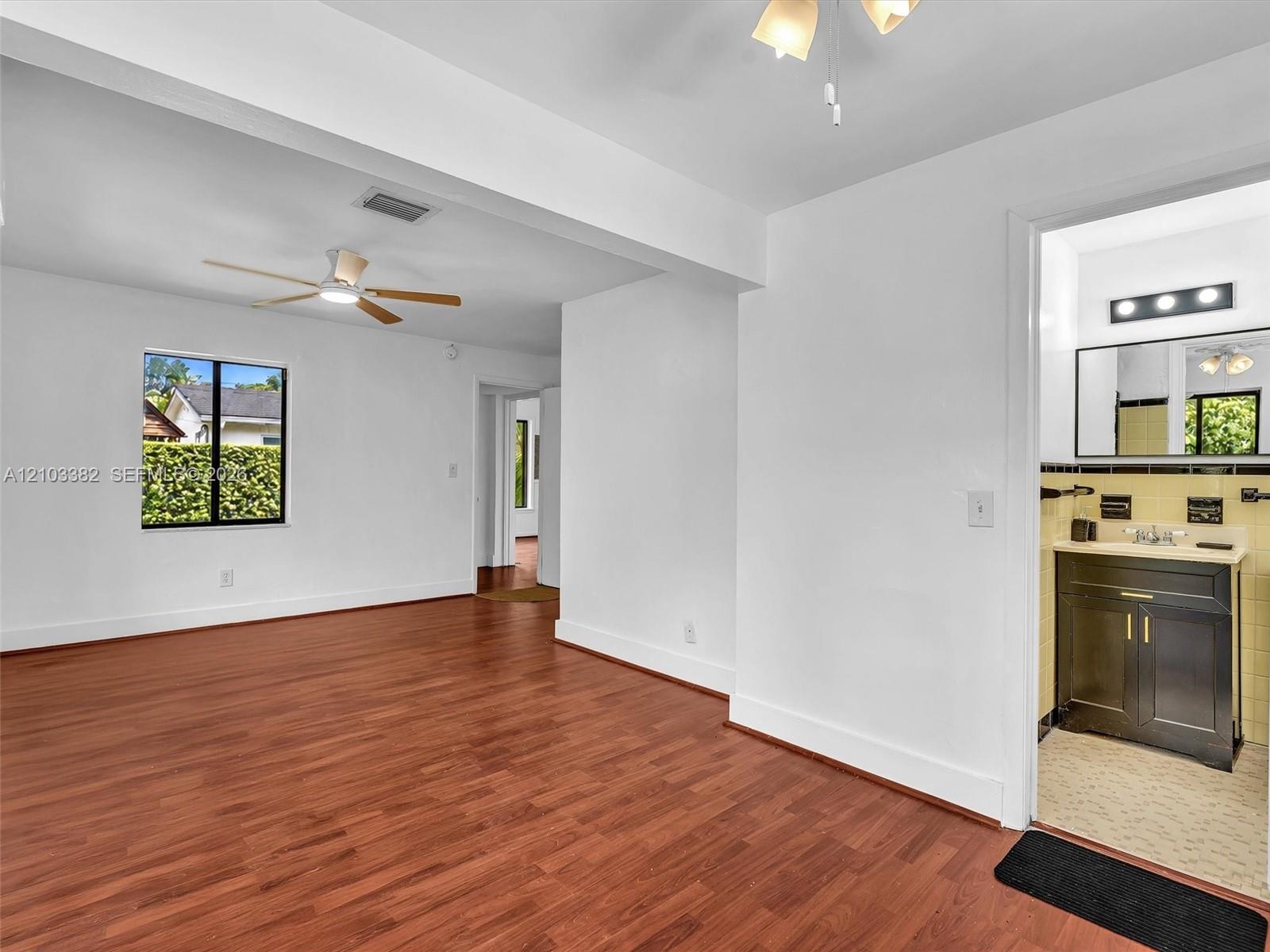Showing seating area in primary bedroom with en suite bath, and walk-in closet. Wood-finish flooring, ceiling fan with integrated lighting, and neutra