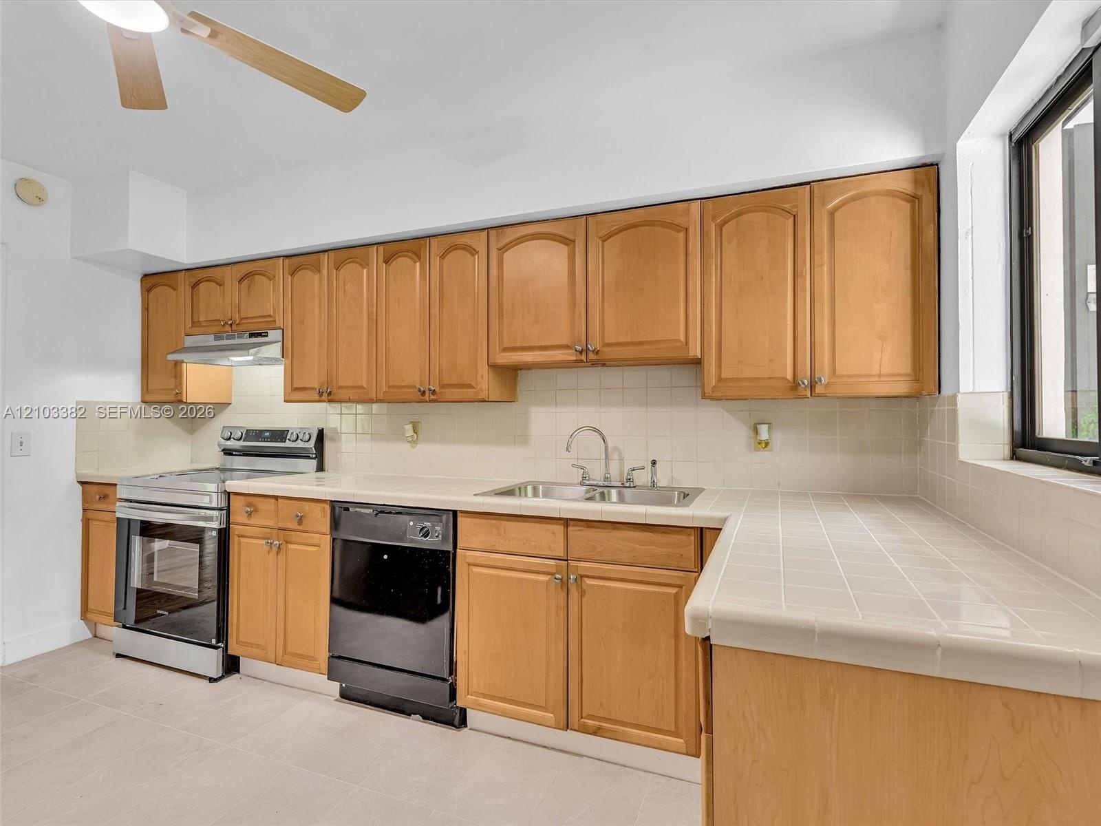 Kitchen featuring tile countertops, tile backsplash, stainless steel range, and integrated ceiling fan. House for rent in Coral Gables. House for rent