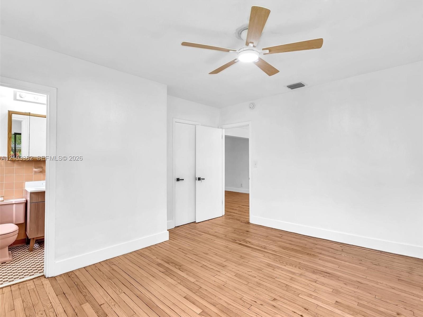West front bedroom with en-suite bath and closet. Wood-finish flooring throughout, ceiling fan with integrated lighting, and white interior doors with