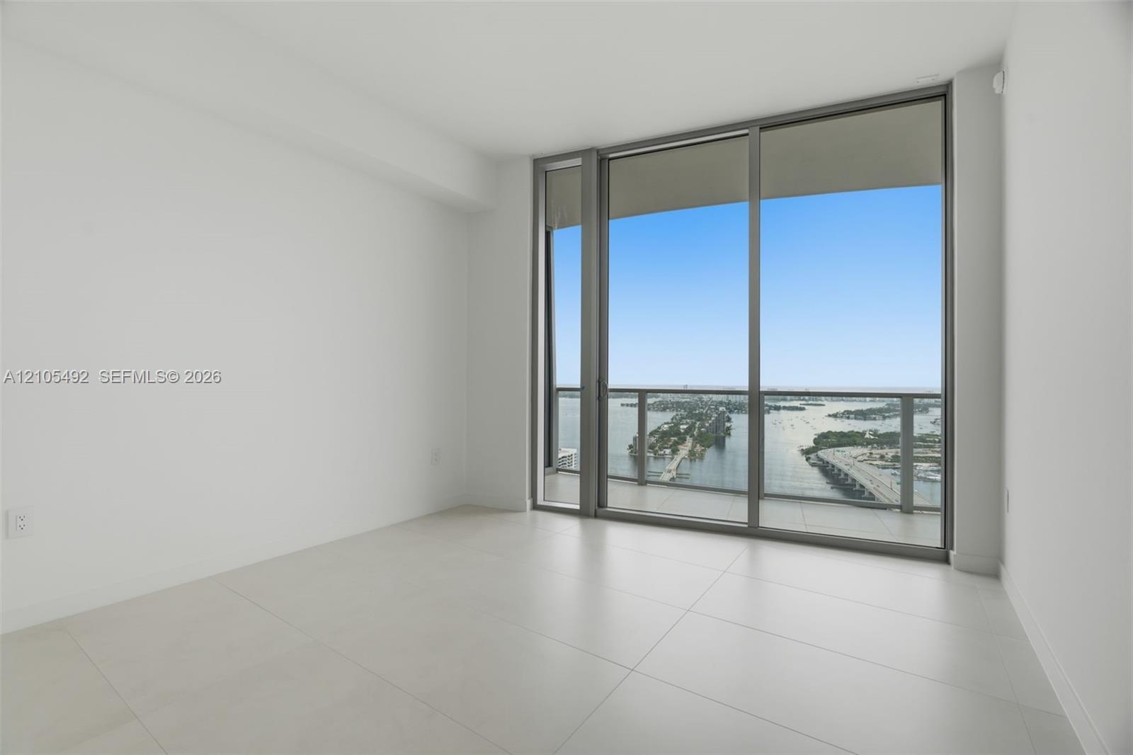Floor-to-ceiling glass windows, large format tile flooring, and a private balcony featuring a metal railing