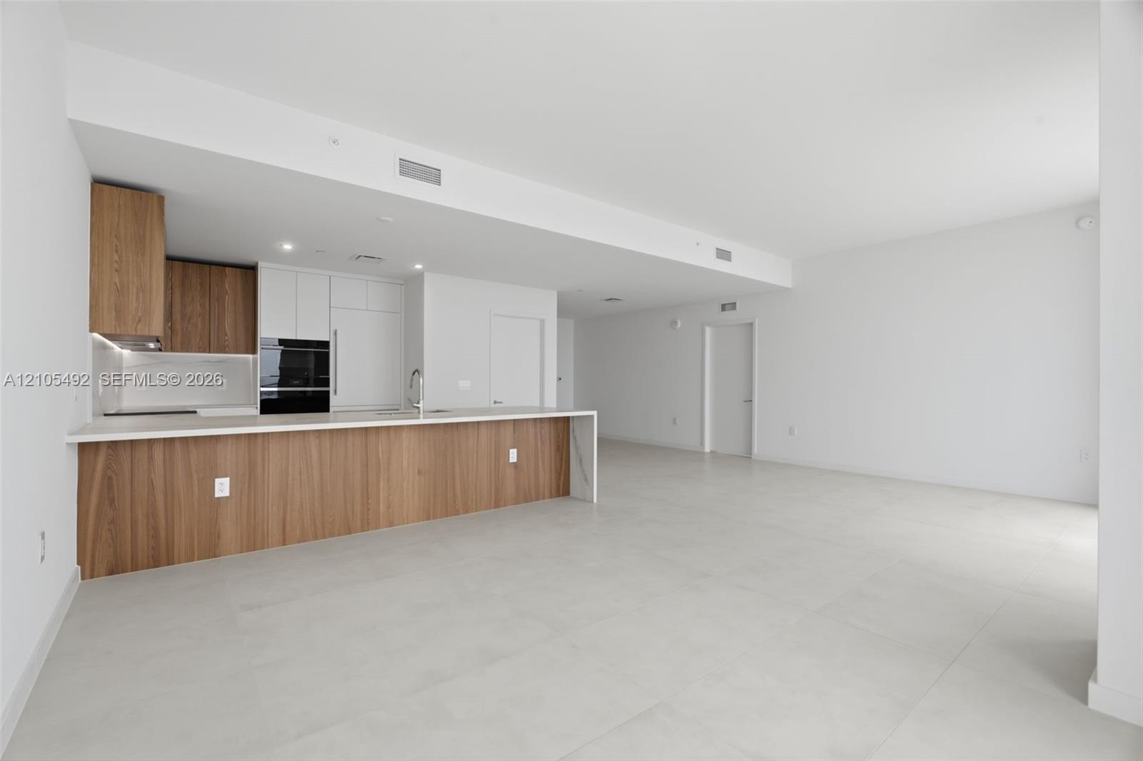 Modern kitchen featuring wood-finish cabinetry, solid-surface countertops, built-in wall oven, and large-format tile flooring