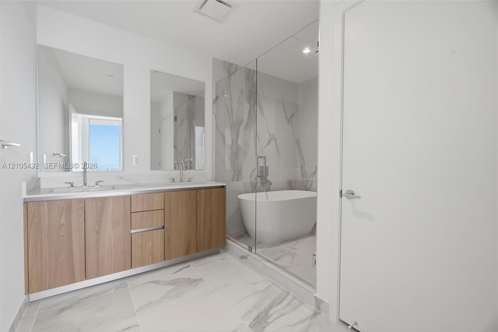 Double vanity featuring wood-finish cabinetry, solid-surface countertops, dual rectangular undermount sinks, and a glass-enclosed wet room with a free