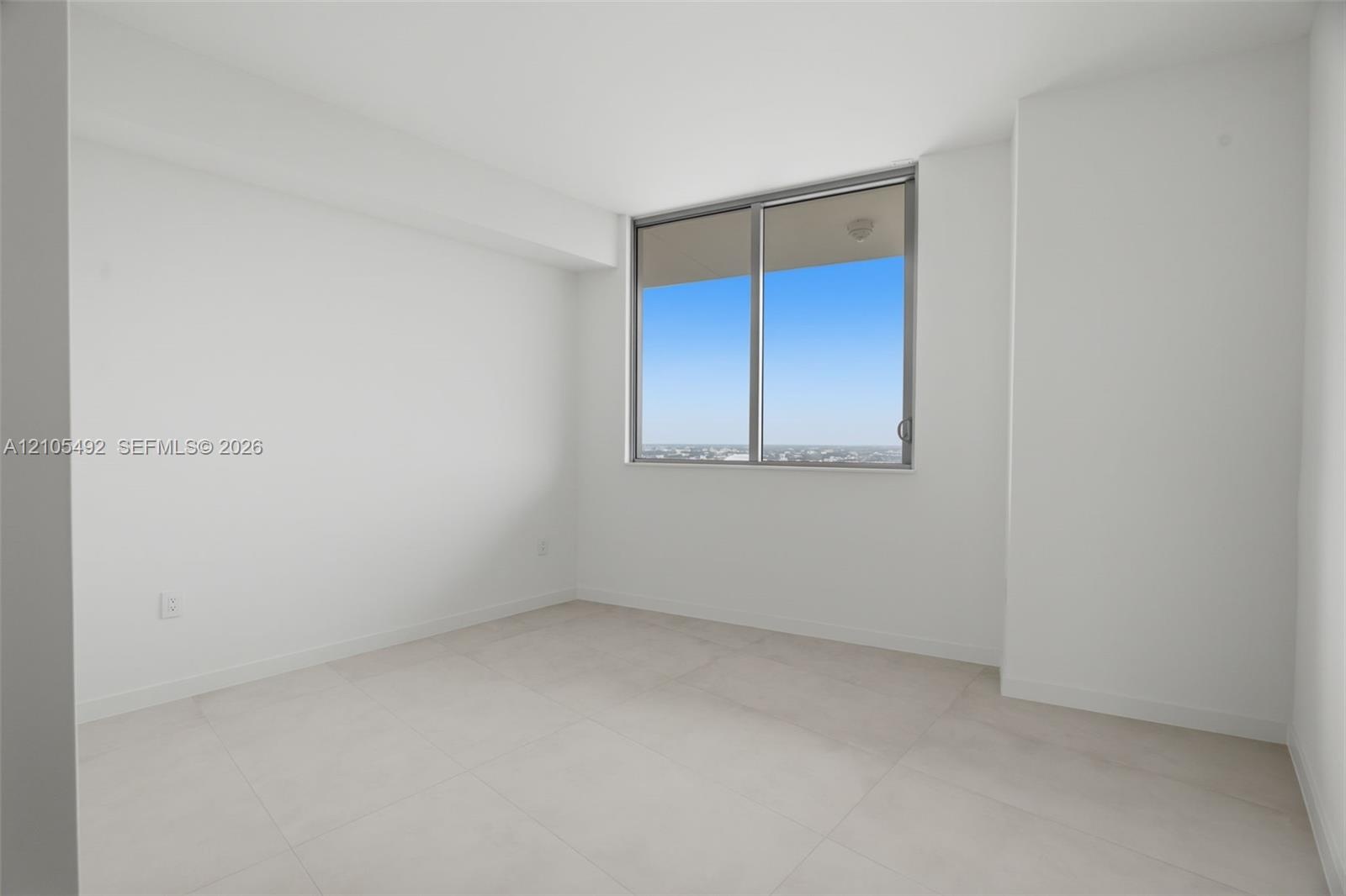 Bright room featuring large-format tile flooring, neutral white walls, and a large sliding glass window with metal framing