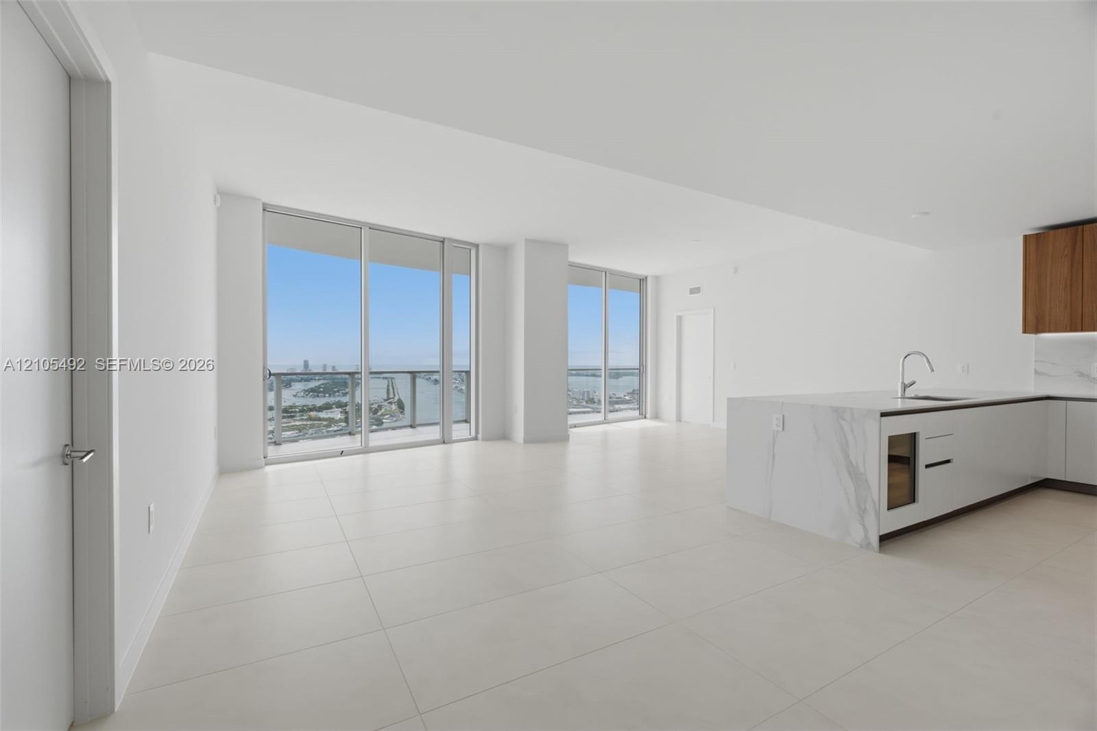 Open-concept living space featuring floor-to-ceiling windows, large-format tile flooring, a kitchen island with stone-finish waterfall countertop, and