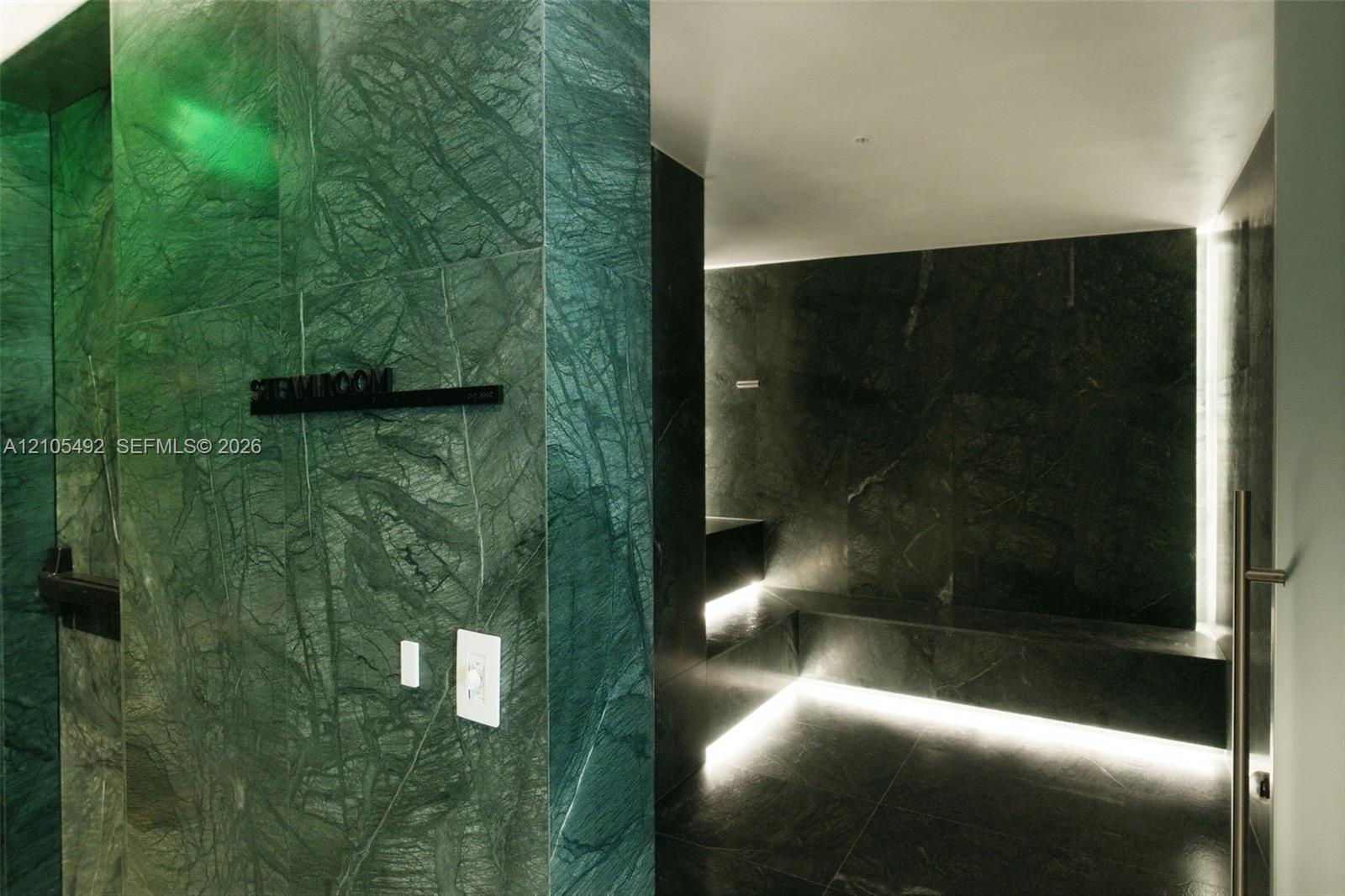 Steam room finished with large-format green stone slab wall cladding, integrated perimeter floor lighting, and built-in stone bench seating