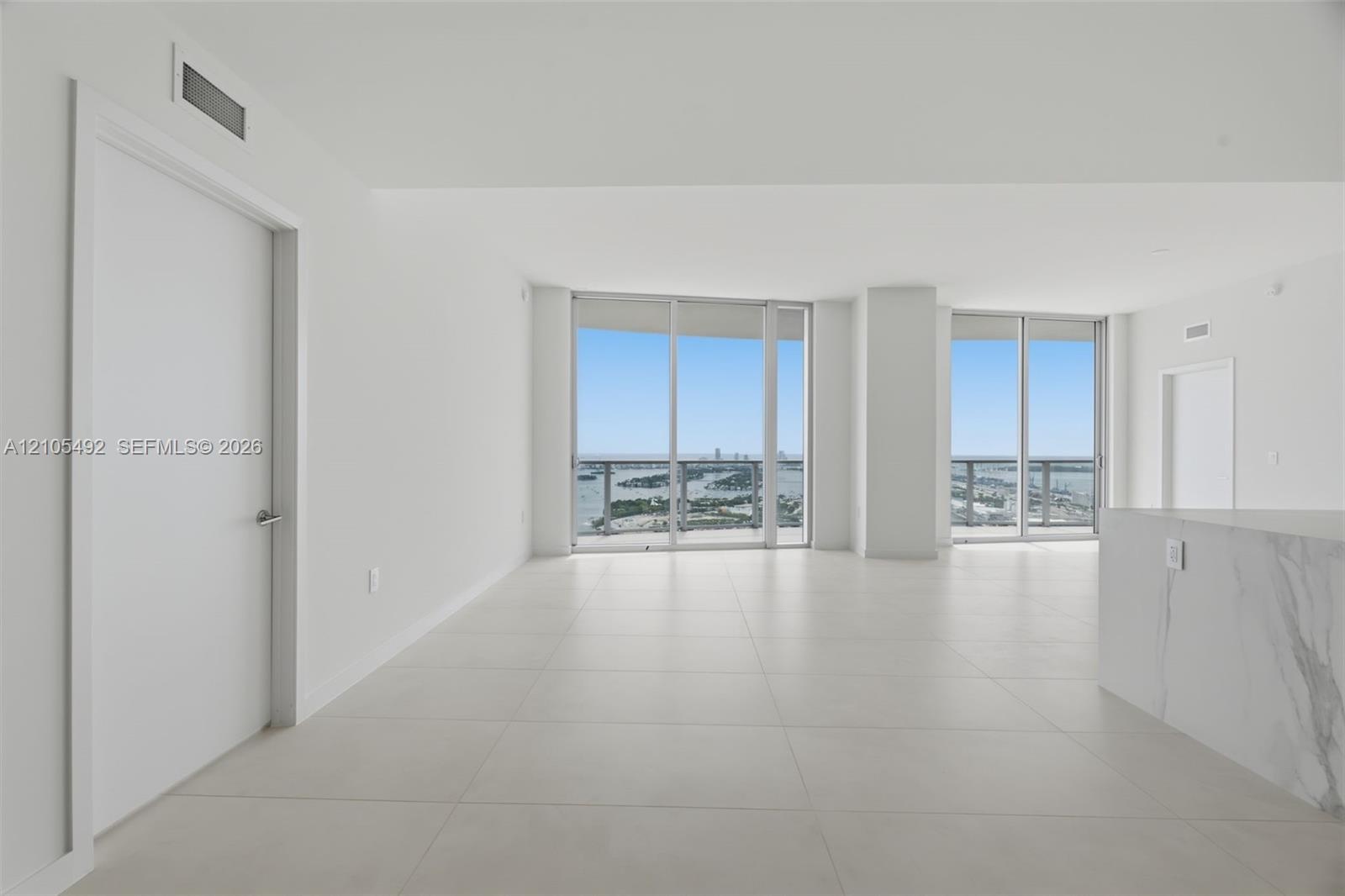 Open-concept interior featuring large-format tile flooring, floor-to-ceiling glass windows, and a built-in stone-finish counter