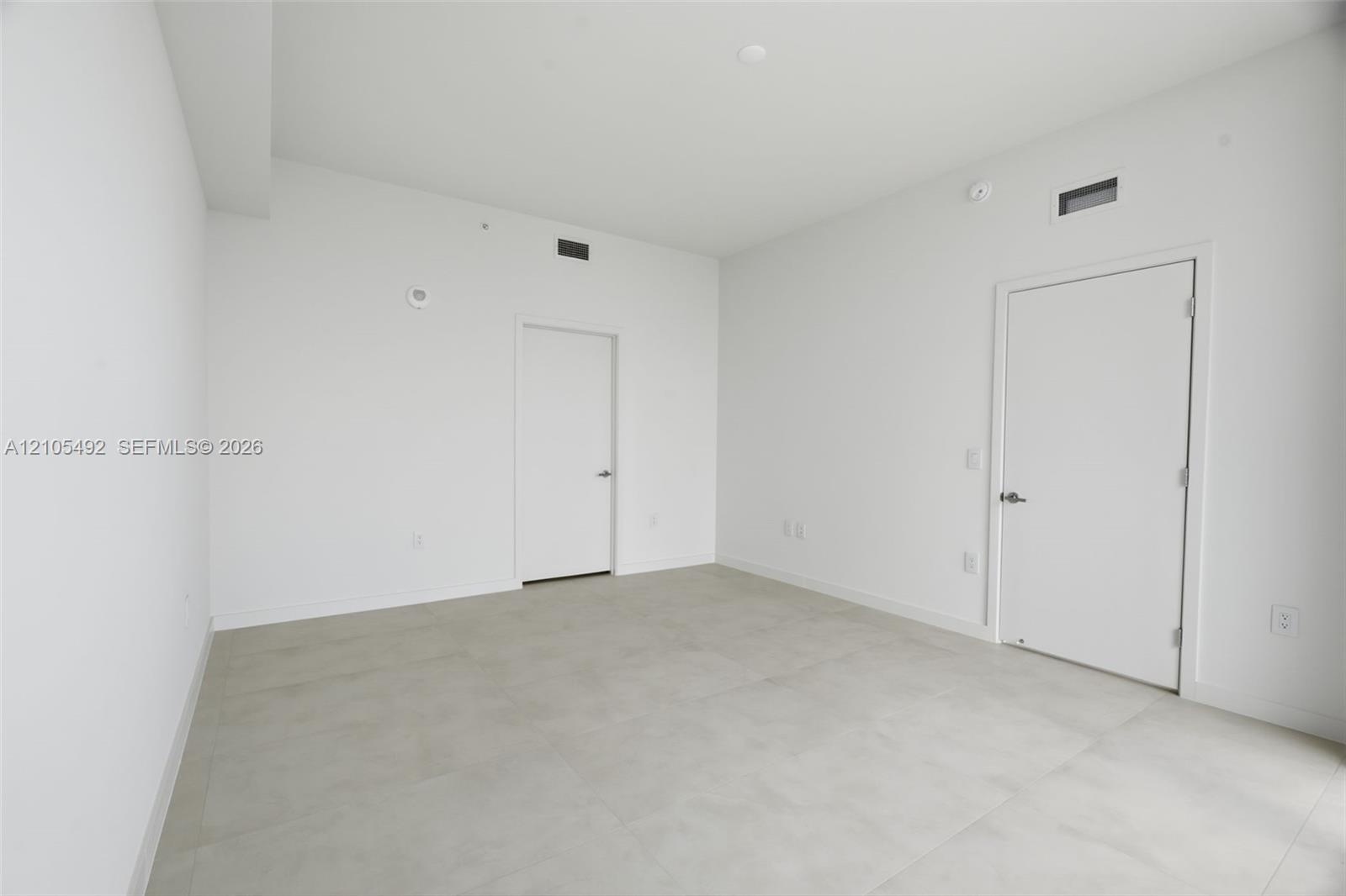 Neutral-toned interior space featuring light-colored large-format tile flooring, white wall finishes, and two solid-core doors