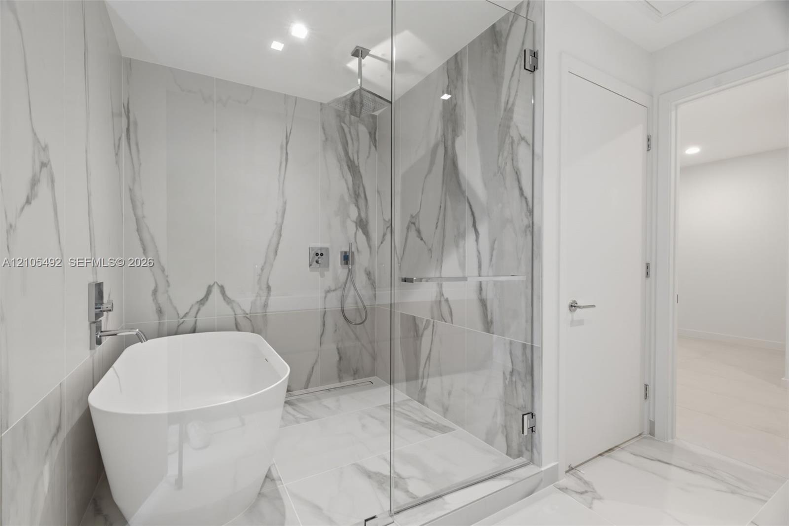 Freestanding soaking tub, frameless glass-enclosed shower, ceiling-mounted rainfall showerhead, and floor-to-ceiling stone-finish tile surround