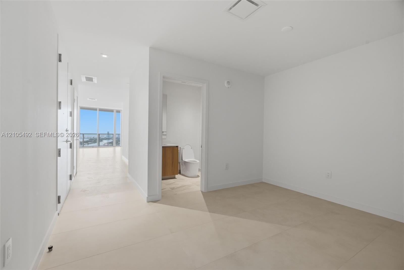 Interior space featuring neutral large-format tile flooring, recessed ceiling lighting, and a bathroom equipped with a wood-finish vanity and integrat
