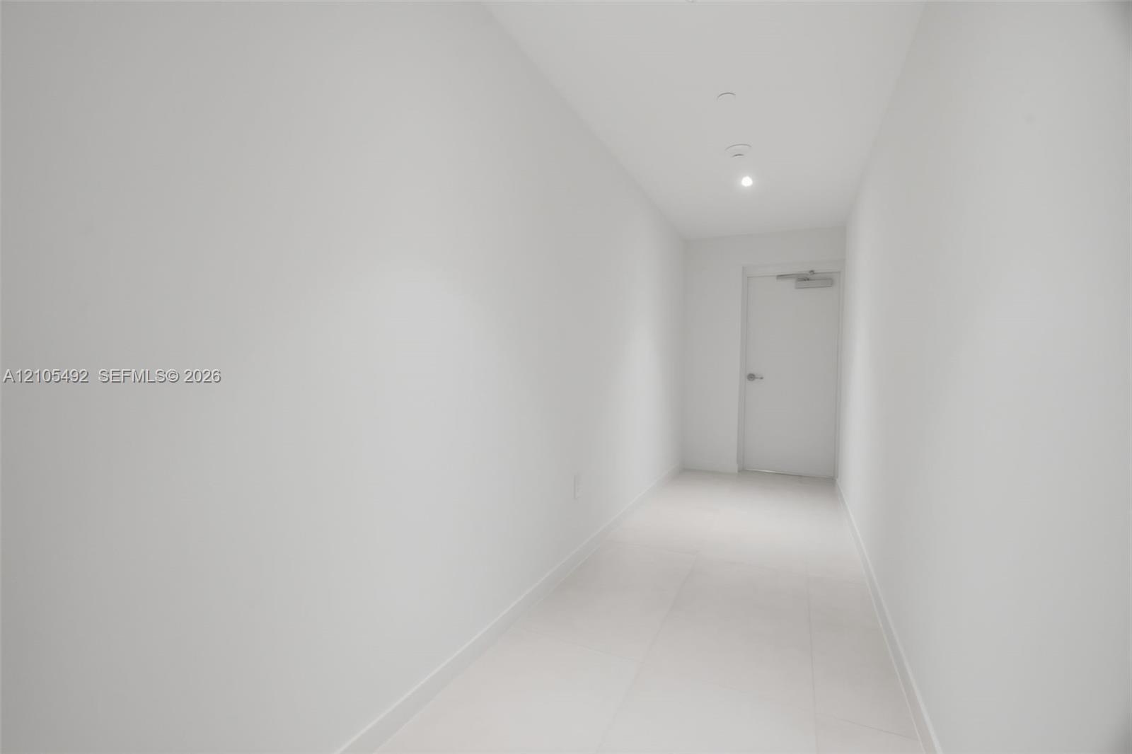 Hallway featuring neutral-toned tile flooring, recessed ceiling lighting, and a solid-core interior door with a silver-finish lever handle