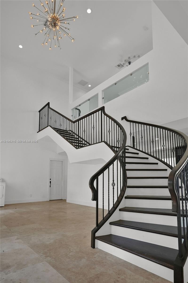 Curved staircase with dark-finished wood treads and metal balusters, polished tile flooring, double-height ceiling, glass-panel balcony railing, and s