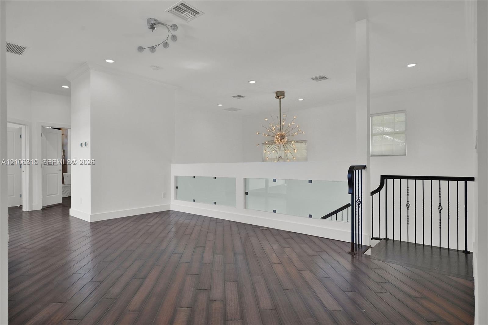 Wood-finish flooring, matte black metal railings, frosted glass safety panels, starburst-style chandelier, and recessed lighting