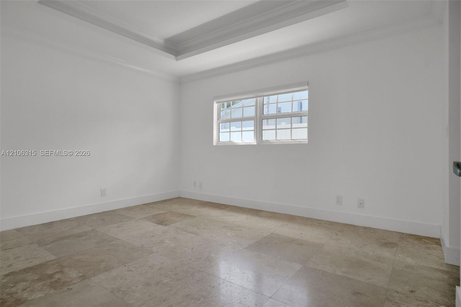 Room featuring a tray ceiling, natural stone tile flooring, and a multi-pane window with a horizontal blind