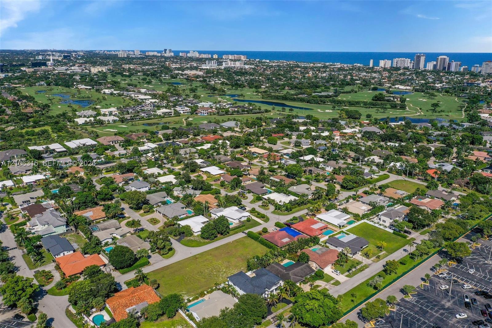 Aerial perspective of a residential neighborhood featuring expansive green space, mature landscaping, and proximity to the coastline