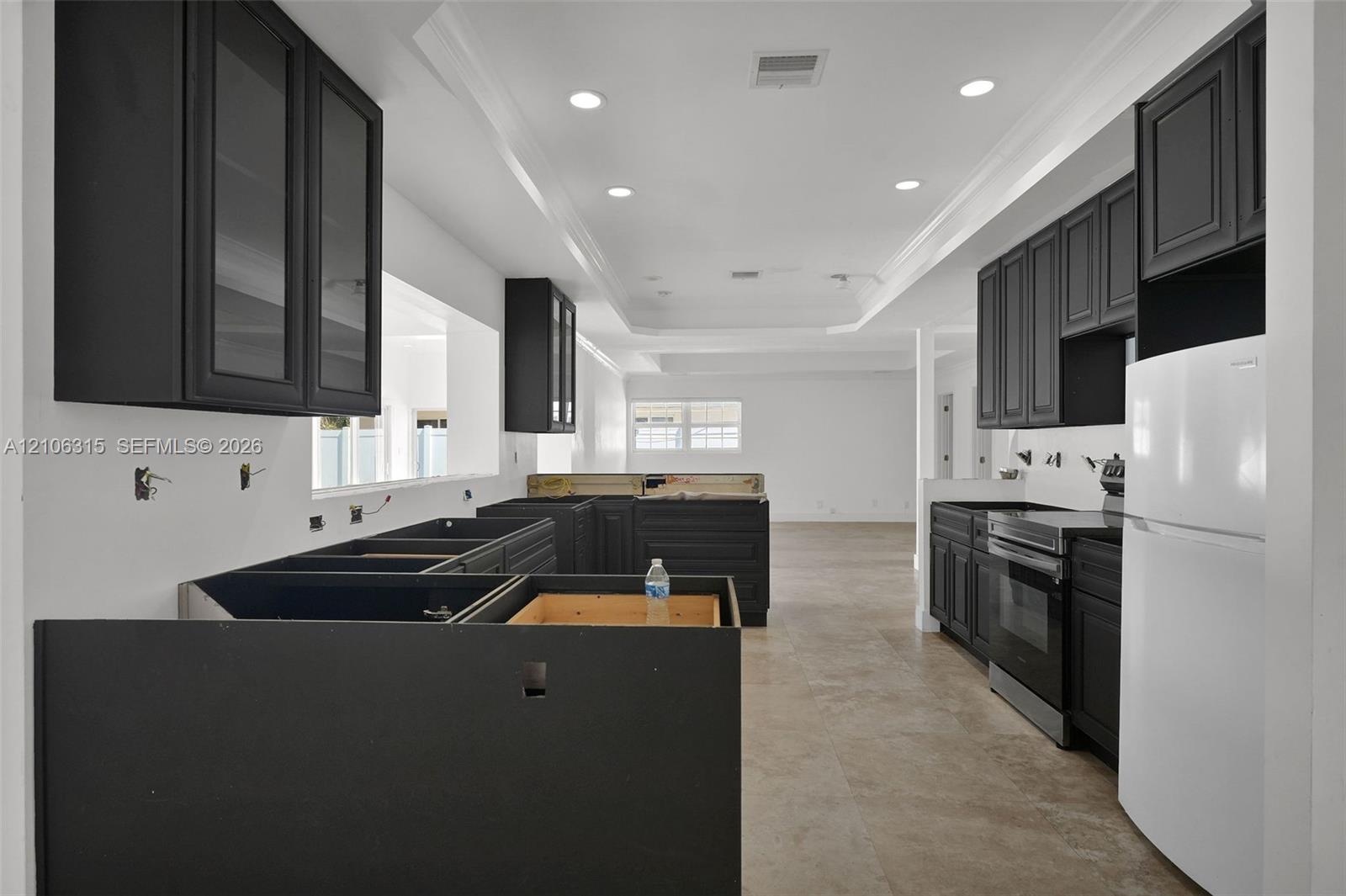 Kitchen featuring dark-toned shaker-style cabinetry, stone flooring, recessed lighting, and crown molding