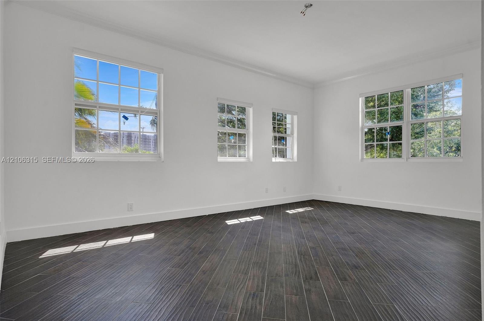 Interior space featuring dark wood-finish flooring, white walls, and multiple multi-pane windows with grid detailing