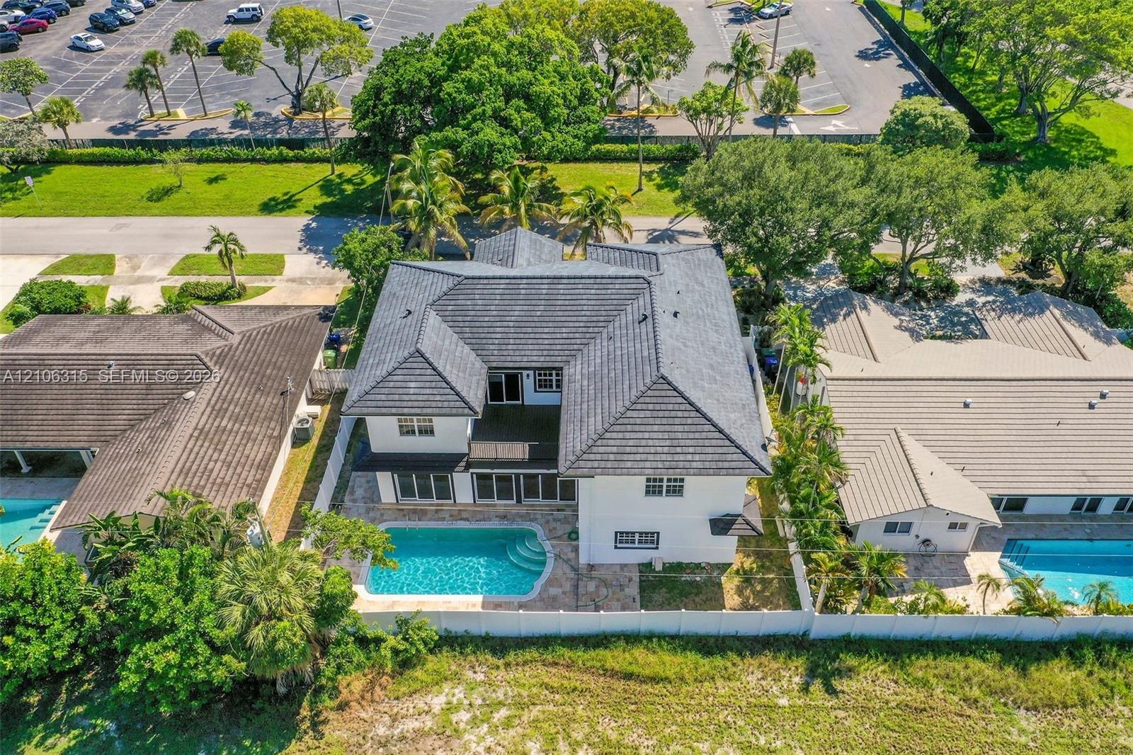 Two-story residence featuring a dark-toned tile roof, exterior stucco finish, private swimming pool, and stone-paver pool deck enclosed by white perim