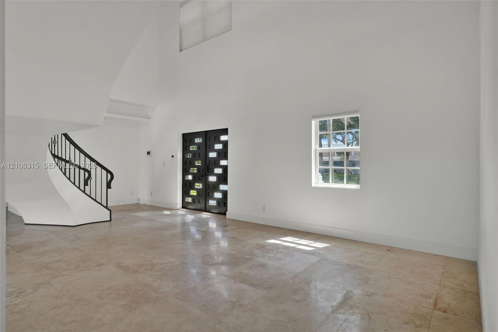 Double-height entry foyer featuring large-format natural stone flooring, a sculptural curved staircase with a black metal railing, and an architectura