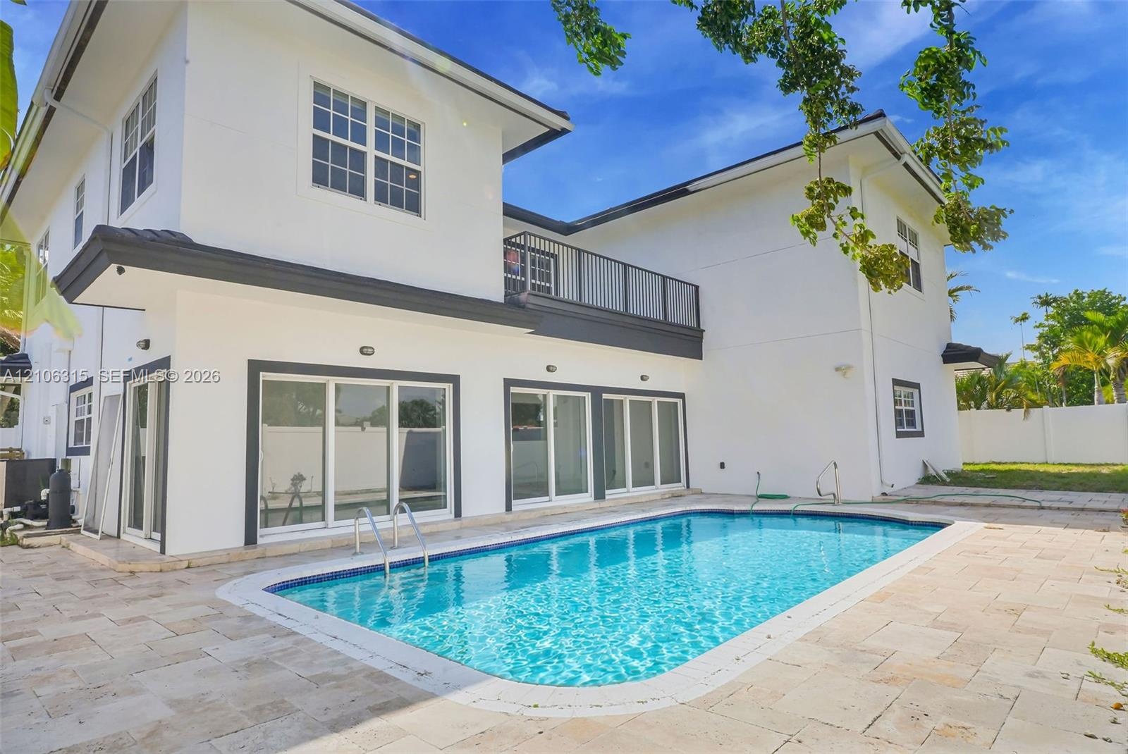 Two-story exterior featuring white stucco finish, second-level balcony with metal railing, multiple sliding glass doors, and a rectangular swimming po