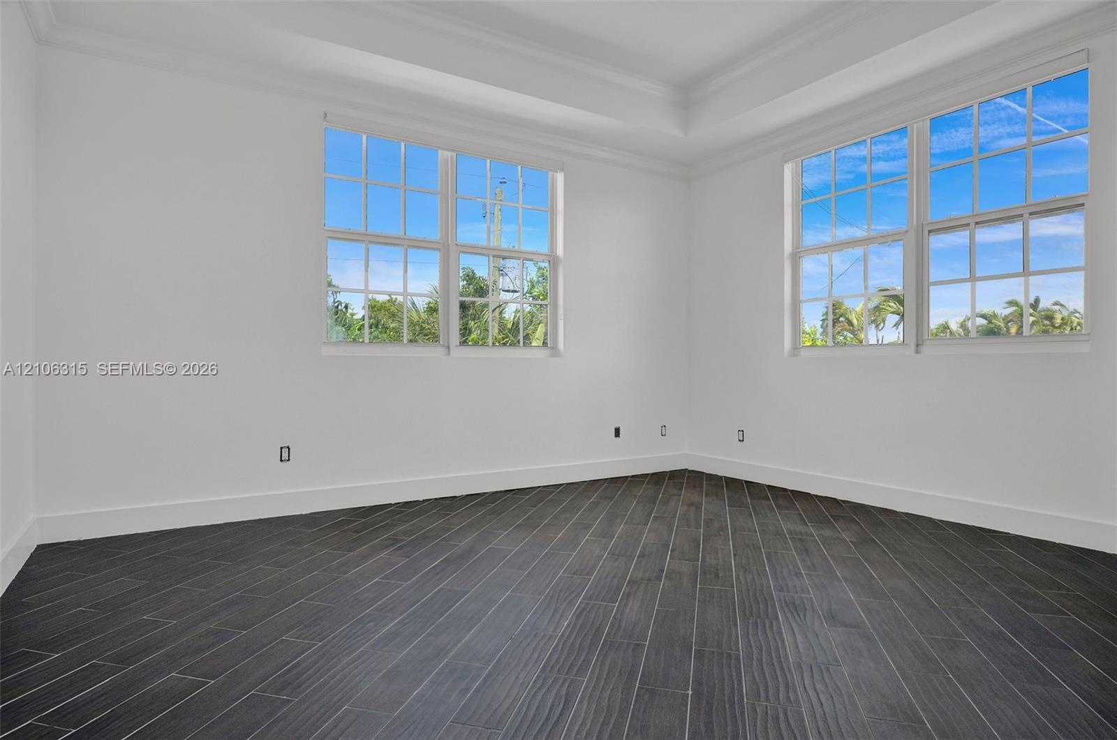 Room featuring dark wood-finish flooring in a herringbone pattern, a tray ceiling, and multi-pane windows