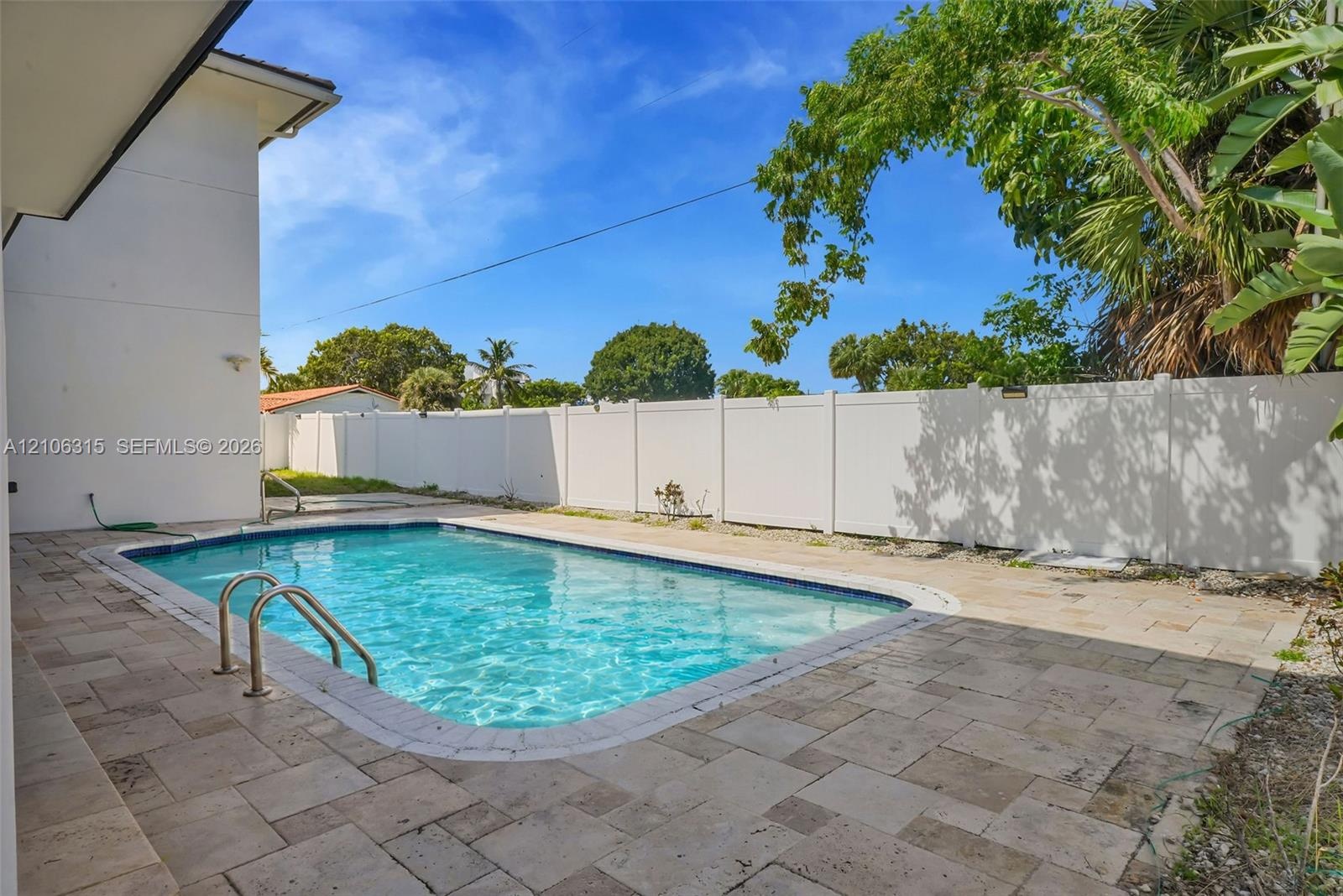 In-ground swimming pool with metal ladder, surrounded by stone paver patio and enclosed by a solid vinyl privacy fence