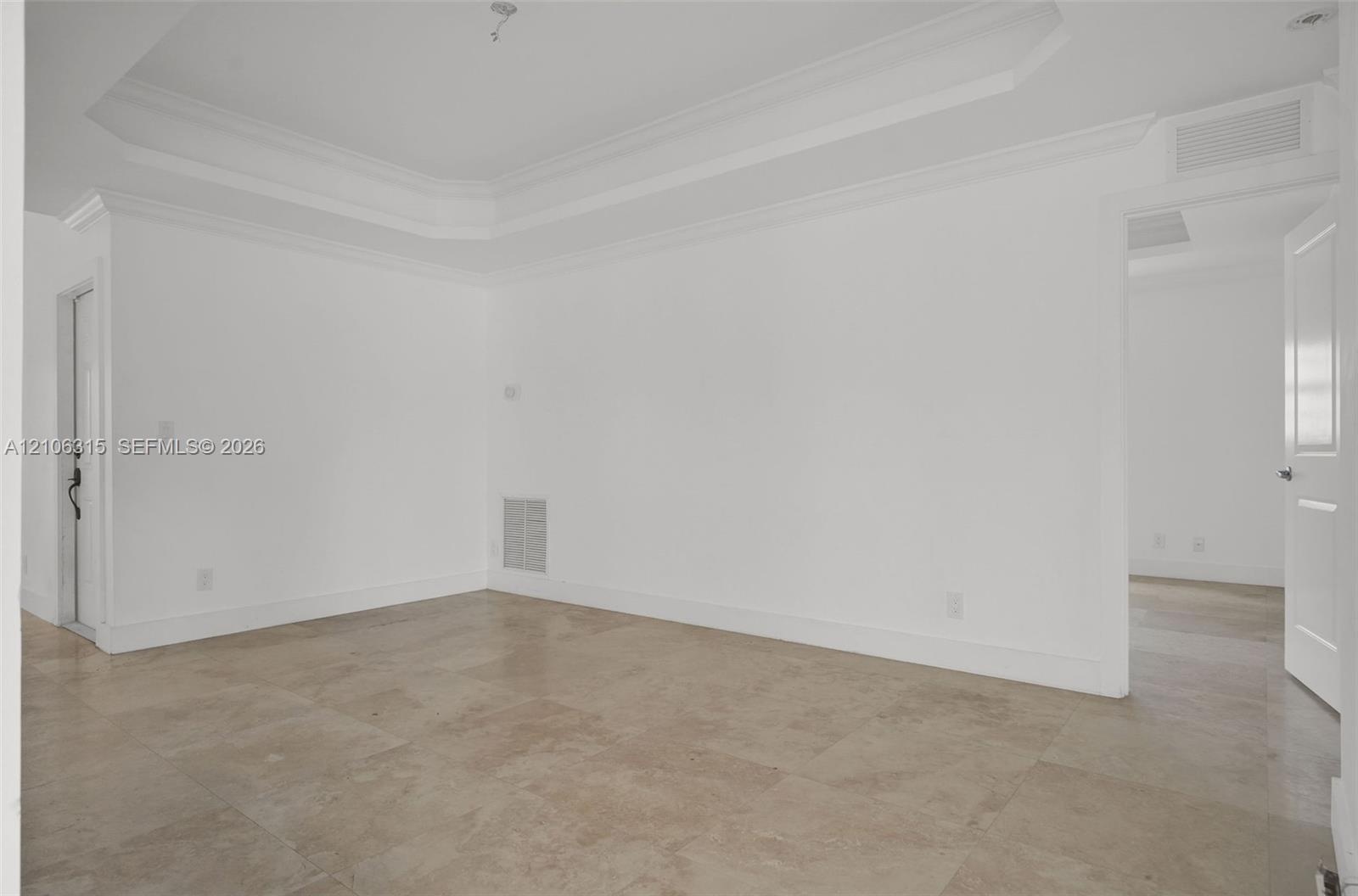 Interior space featuring a recessed tray ceiling, crown molding, and large-format neutral tile flooring