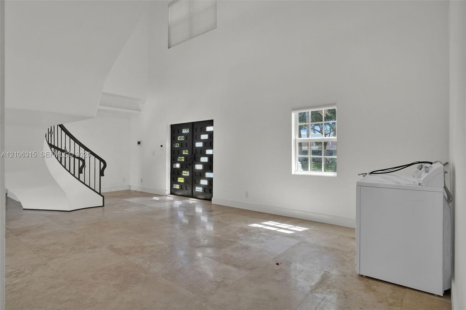 Double-height foyer featuring stone tile flooring, a curved staircase with a metal handrail, and a decorative double entry door with glass paneling