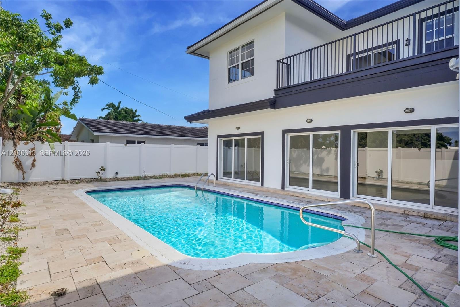 Exterior featuring a white stucco facade, private swimming pool, stone paver decking, white vinyl perimeter fencing, and an upper-level balcony with m