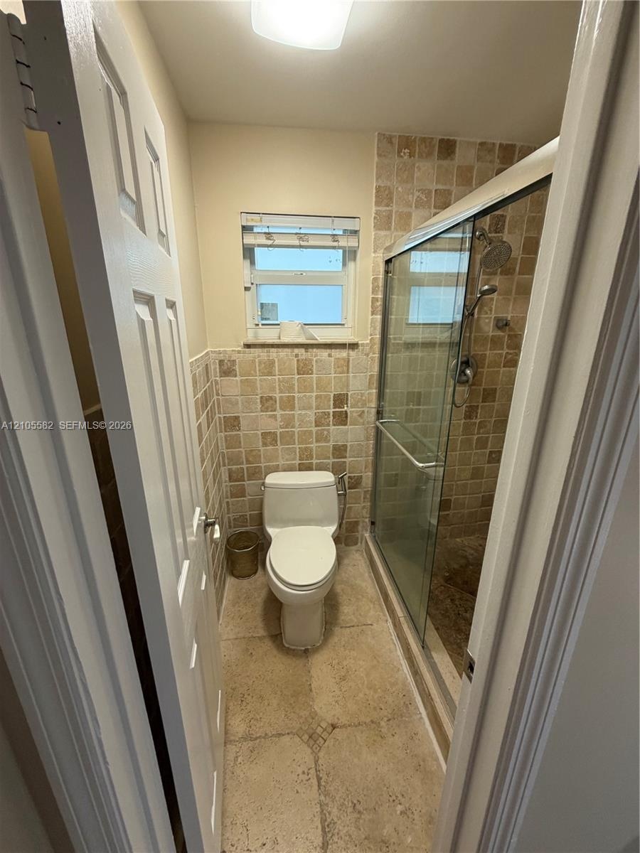Tiled shower enclosure with a glass door, wall-mounted showerhead, and a window for natural light