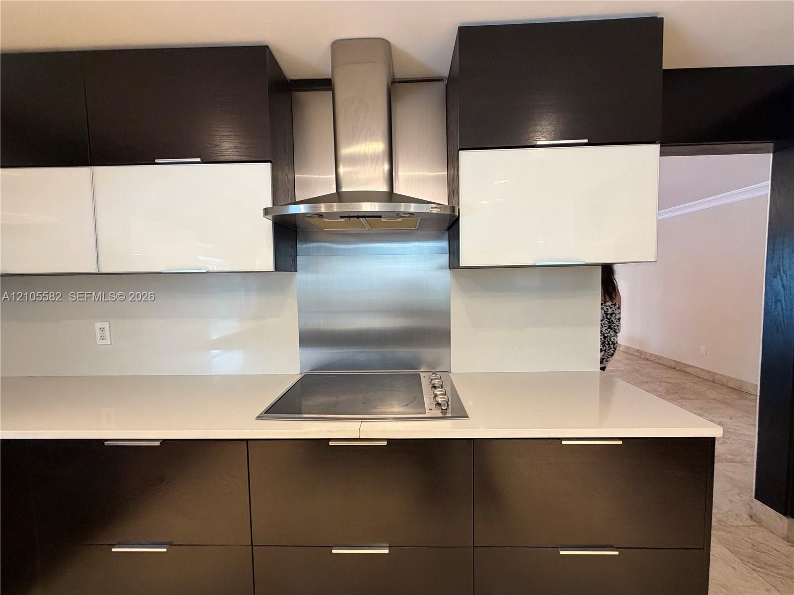 Integrated cooktop with stainless steel range hood, white countertop, and two-tone cabinetry