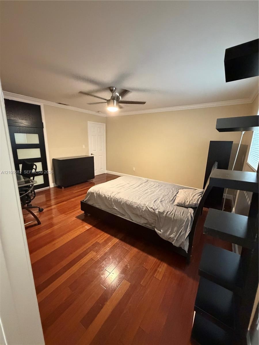 Hardwood flooring throughout, ceiling fan with integrated lighting, crown molding, and a solid door with horizontal glass panels