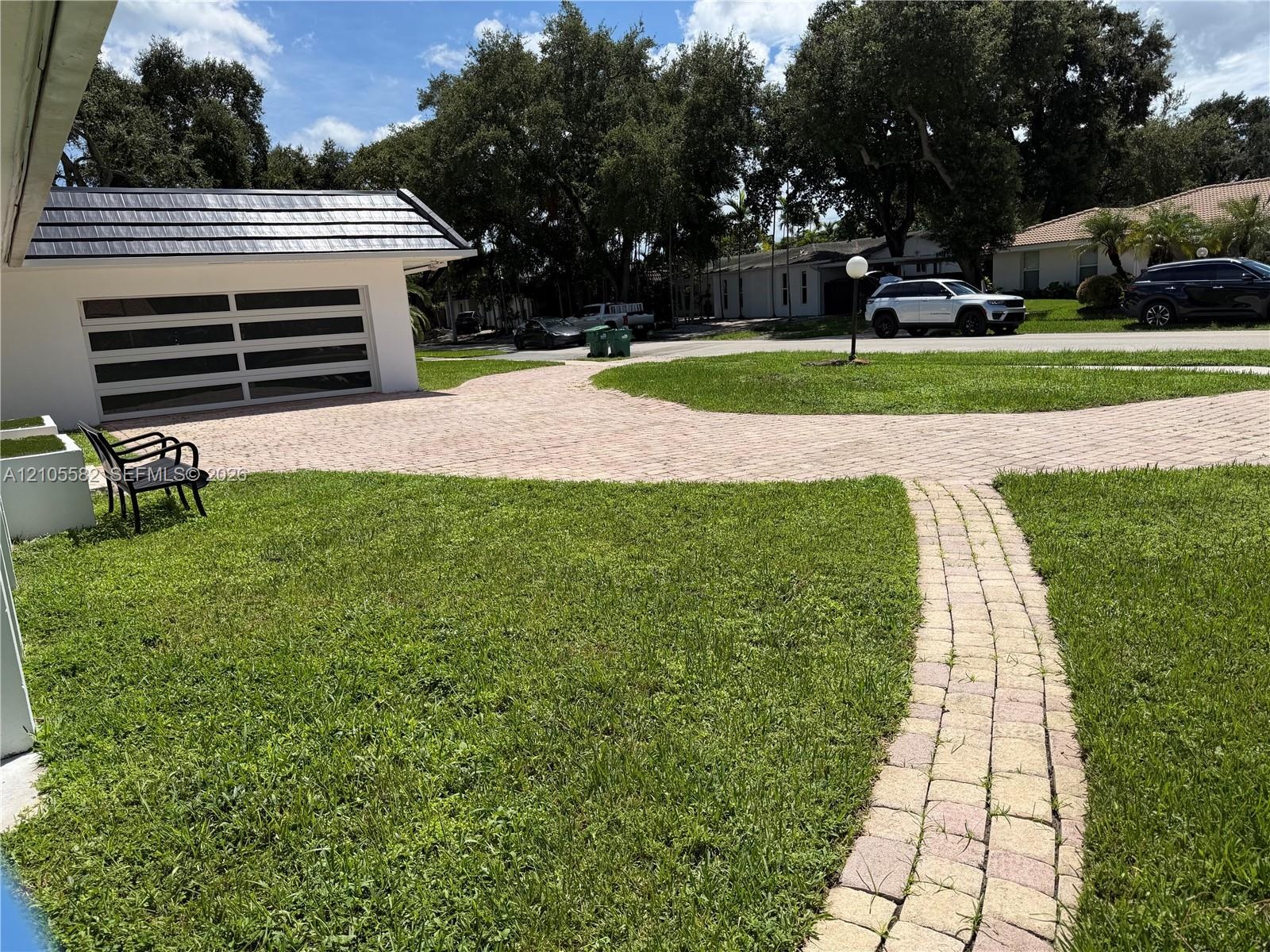 Paved driveway leading to a modern garage door with frosted glass panels, featuring a distinct dark-tiled roof