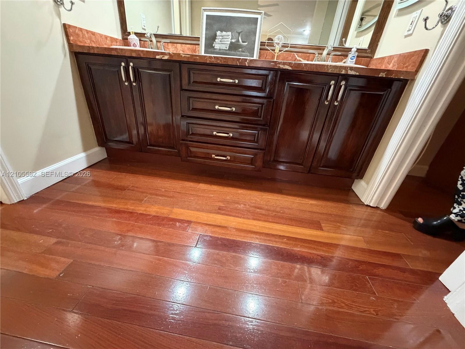 Dual vanity with a stone countertop, dark wood-finish cabinetry, and wood-finish flooring