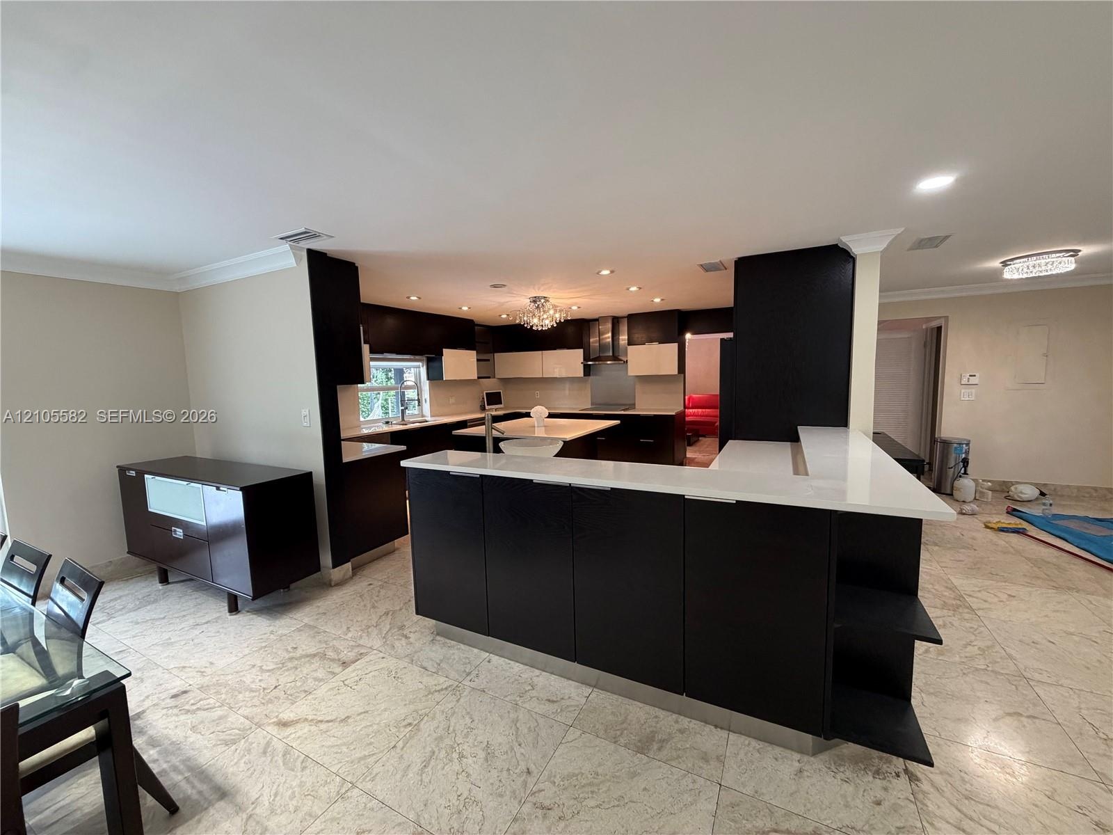 Open-concept kitchen featuring an island with white countertops, dark wood-finish cabinetry, recessed lighting, and tile flooring throughout