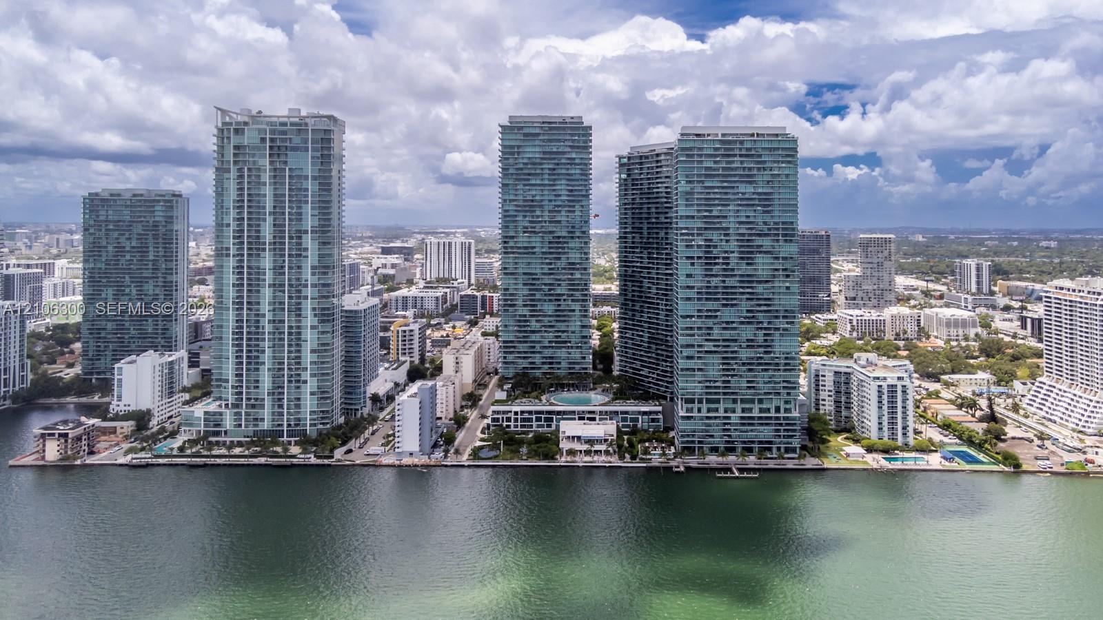 High-rise waterfront complex featuring glass-facade towers, a central swimming pool, and extensive manicured landscaping