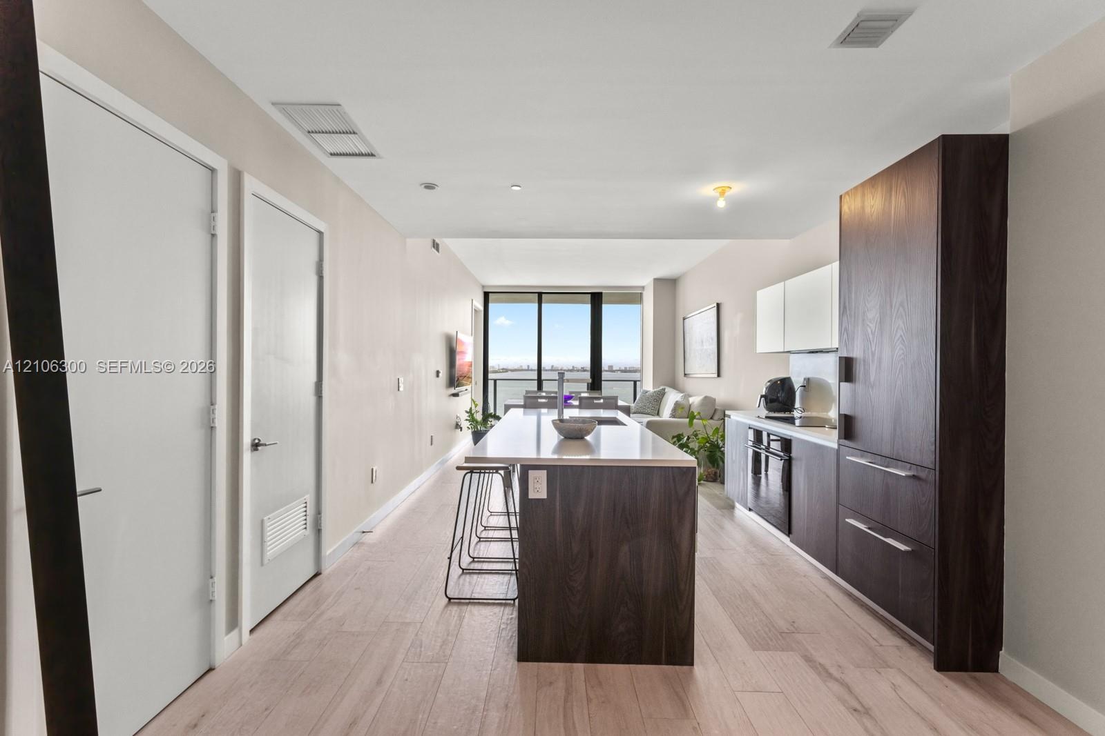 Kitchen featuring a central island with a solid-surface countertop, dark wood-finish cabinetry, built-in appliances, and light wood-finish flooring th