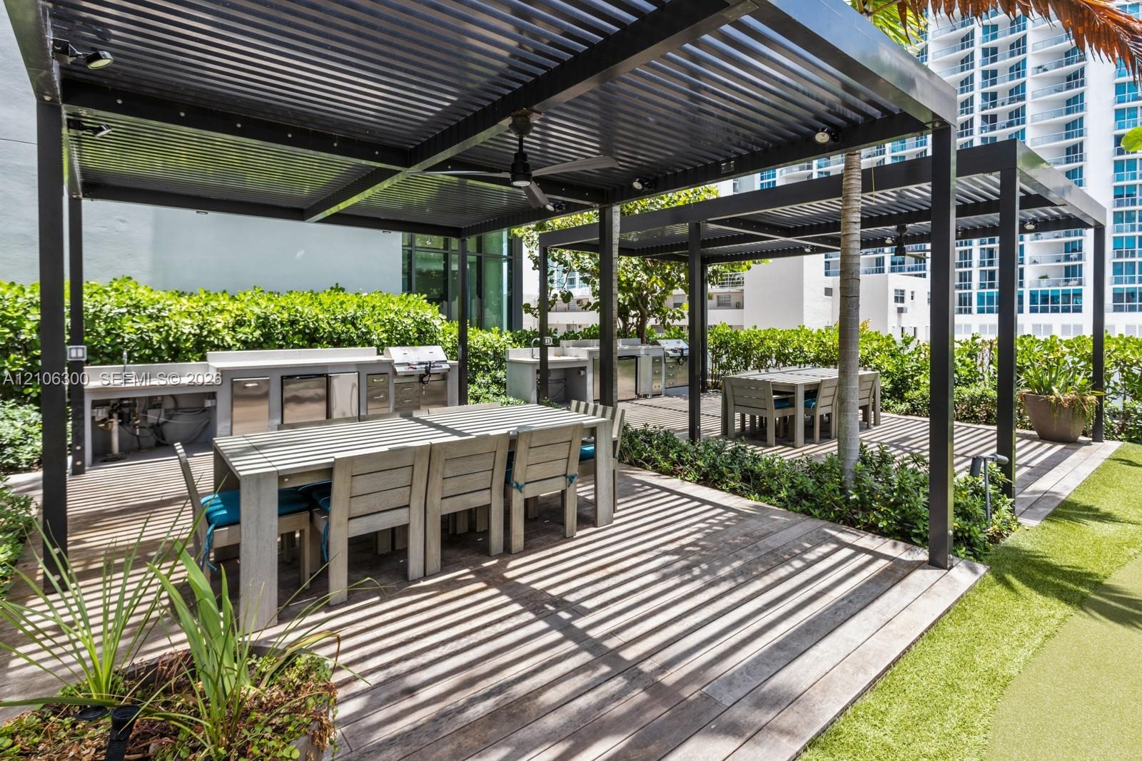 Outdoor kitchen featuring stainless steel appliances, dual metal pergolas, wood-finish decking, and built-in stone-finish counters