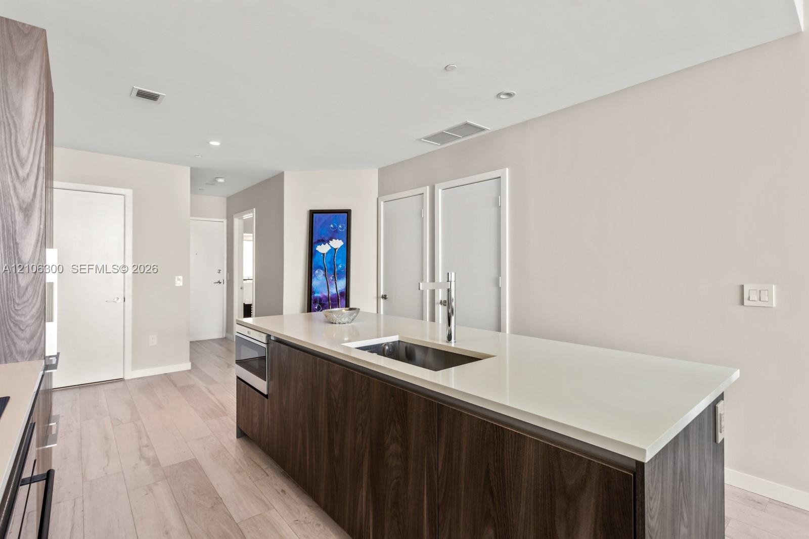 Kitchen island featuring dark wood-finish cabinetry, a white countertop, an integrated stainless steel undermount sink, and a high-arc faucet, complem